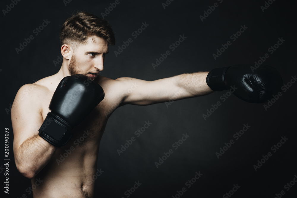 Side view portrait of a young man wearing boxing gloves and training in a studio.
