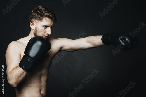 Side view portrait of a young man wearing boxing gloves and training in a studio.
