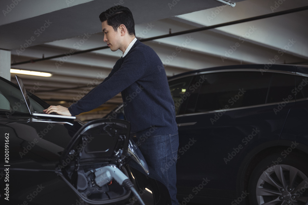 Man using laptop while charging electric car Man using laptop while charging electric car