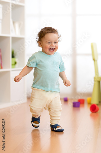 First steps of baby toddler learning to walk in living room. Footwear for little children.