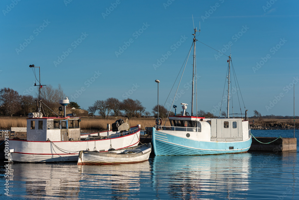 Obraz premium Old and well used fishing boats moored in harbor on a spring evening in Gronhogen on Oland, Sweden. Names and logos removed.