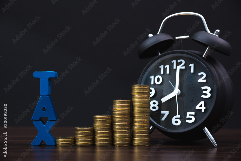 Time to pay TAX concept. TAX alphabet with stack of coin and vintage alarm clock in dark background, business and financial concept. Time to pay TAX concept. TAX alphabet with stack of coin and vintage alarm clock in dark background, business and financial concept.