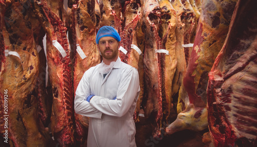 Portrait of butcher standing with arms crossed in meat storage room photo