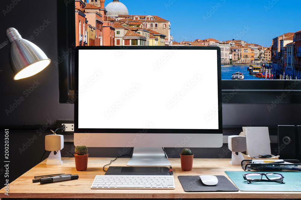 Naklejka premium Graphic designer's workspace with a pen tablet, a computer and white screen for text with beautiful Venice cityscape view from the window