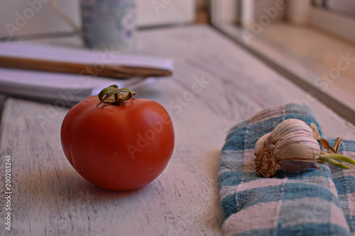Closeup of organic red tomato whit garlic, open cookbook and wooden spoon at light wooden background