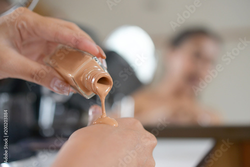 Asian woman applying foundation on her face for beauty.
