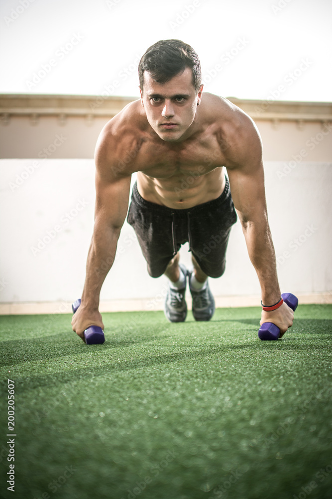 Handsome muscular young man doing push up exercise with weights outdoors