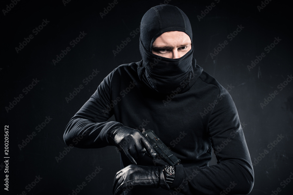 Male criminal in gloves with gun checking his watch Male criminal in gloves with gun checking his watch