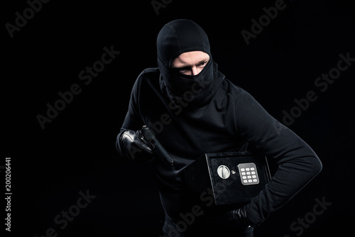 Burglar in balaclava holding gun and locked safe