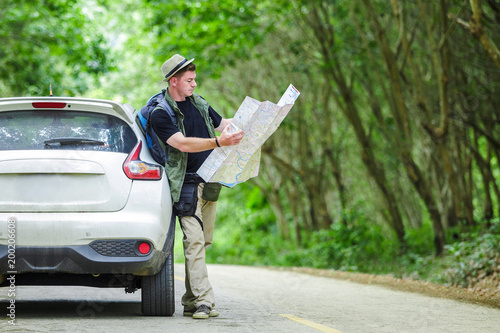 Young man driving car on to the road tree. Traveler with backpack looking map.