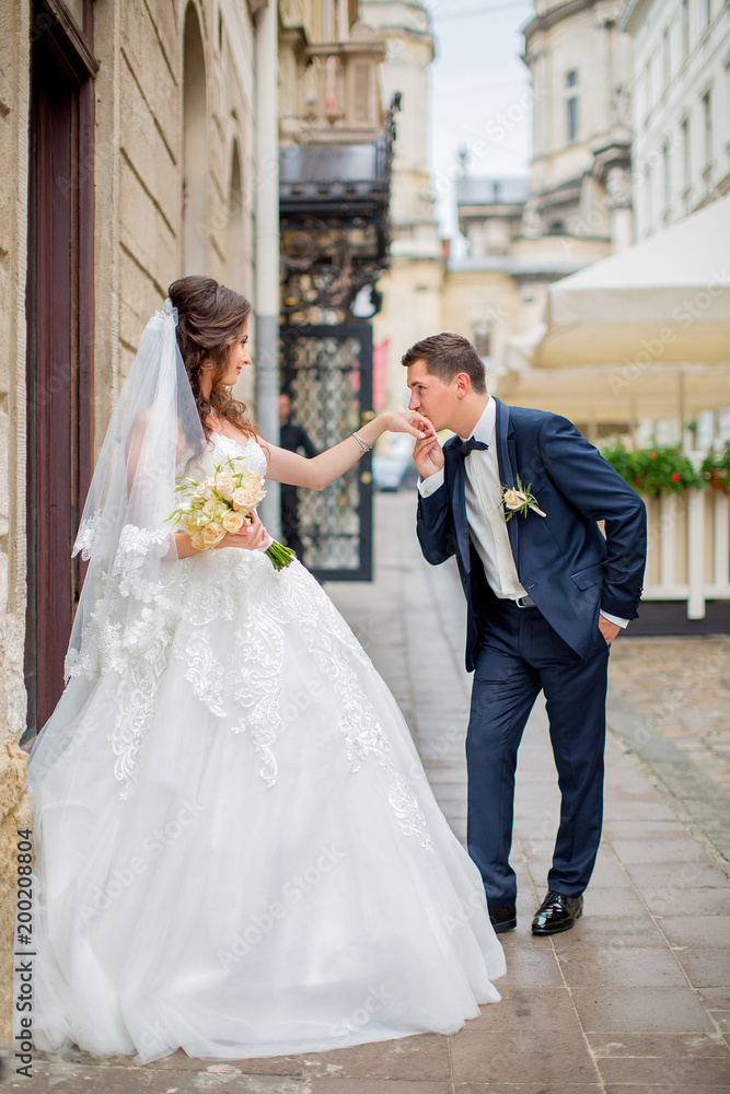 Groom kisses hand of beautiful bride, on background of old street of Lviv, Ukraine