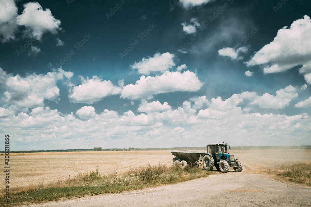 Tractor With Cart In Motion On Country Road In Summer Season. Agricultural Landscape Tractor With Cart In Motion On Country Road In Summer Season. Agricultural Landscape