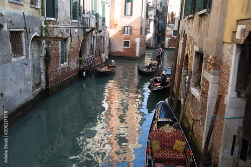 Narrow Venice cityscape with water canal, old houses, gondolas and gondolier punting across