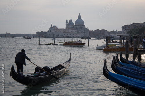 Gondolier punting gondola boat in a lagoon with Santa Maria della Salute (Saint Mary of Health) in a background photo