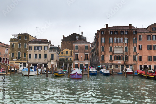 Various boats parked on the Grand Canal pier in front of old residential buildings in Venice, Italy on a rainy and cloudy day