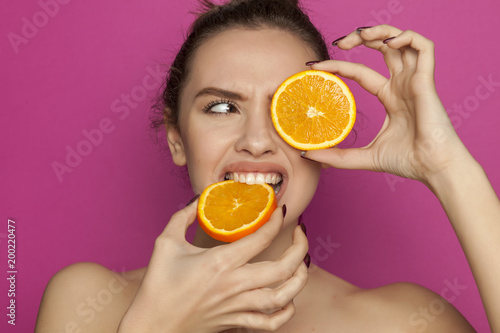 Young sexy woman eatin slices of oranges on pink background