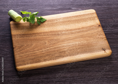 Wooden kitchen cutting Board on dark wooden background with greenery.