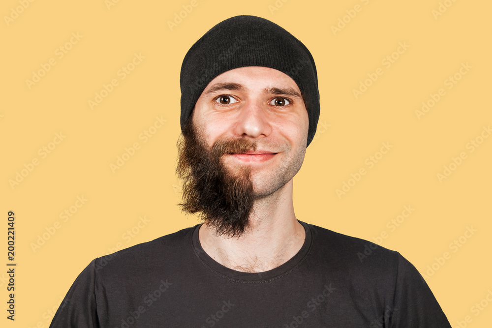 Young guy in hat with half shaved beard smiled. Isolated on orange background. Young guy in hat with half shaved beard smiled. Isolated on orange background.