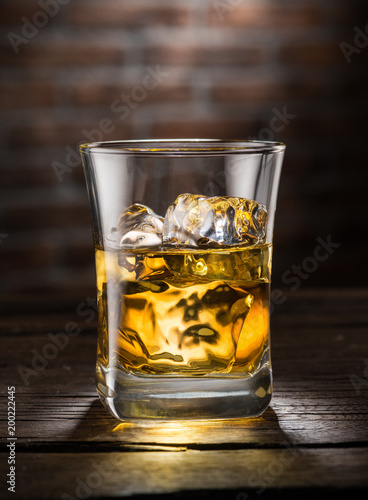 Whiskey glass or glass of whiskey with ice cubes on the wooden background.