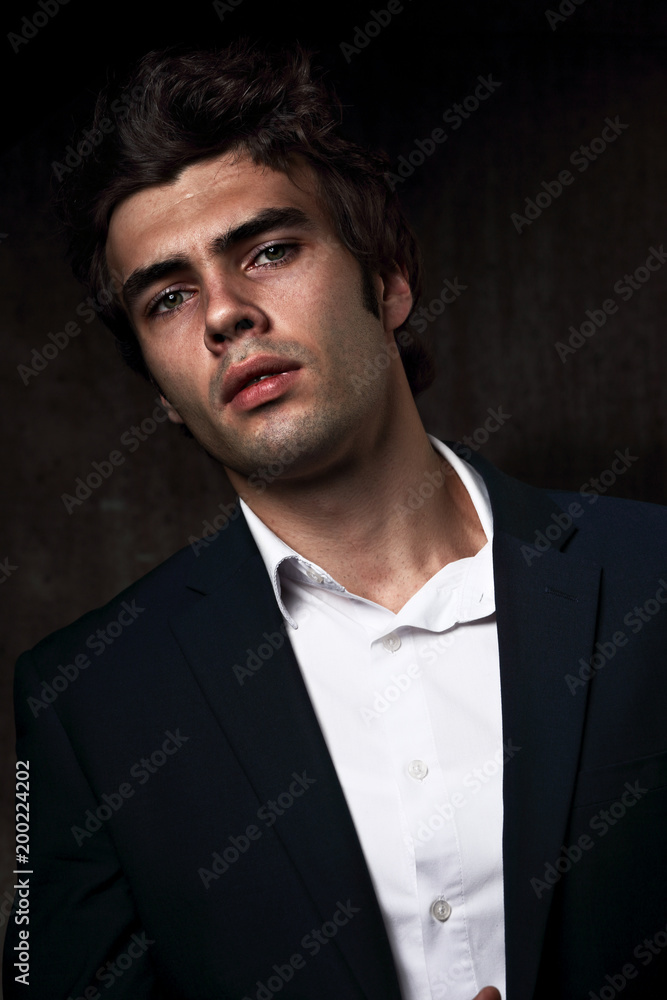 Sexy serious male business model posing in blue suit and white style shirt on dark shadow background. Fashion style vogue portrait Sexy serious male business model posing in blue suit and white style shirt on dark shadow background. Fashion style vogue portrait