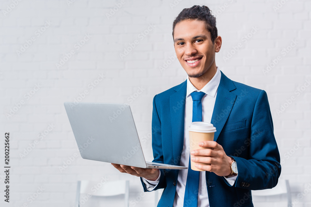 Smiling businessman holding laptop and coffee cup Smiling businessman holding laptop and coffee cup