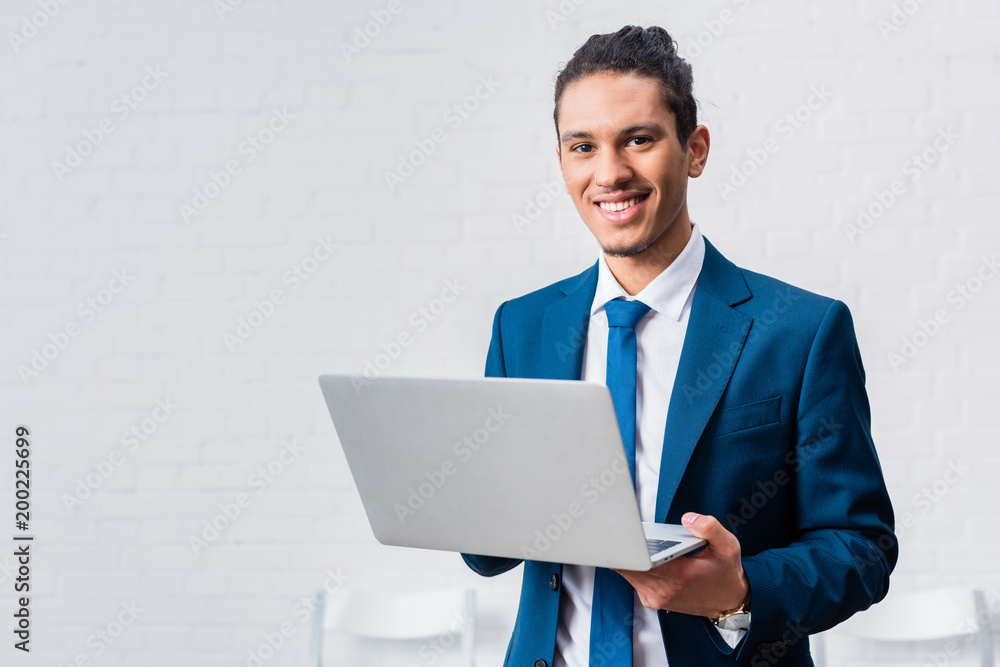 Smiling businessman holding laptop on white wall background Smiling businessman holding laptop on white wall background