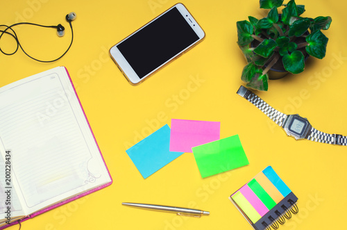 working space with a notebook, pen, clock, telephone, headphones on a yellow background. place for text. The working space of a freelancer, journalist, writer. On a bright yellow background. Top view.