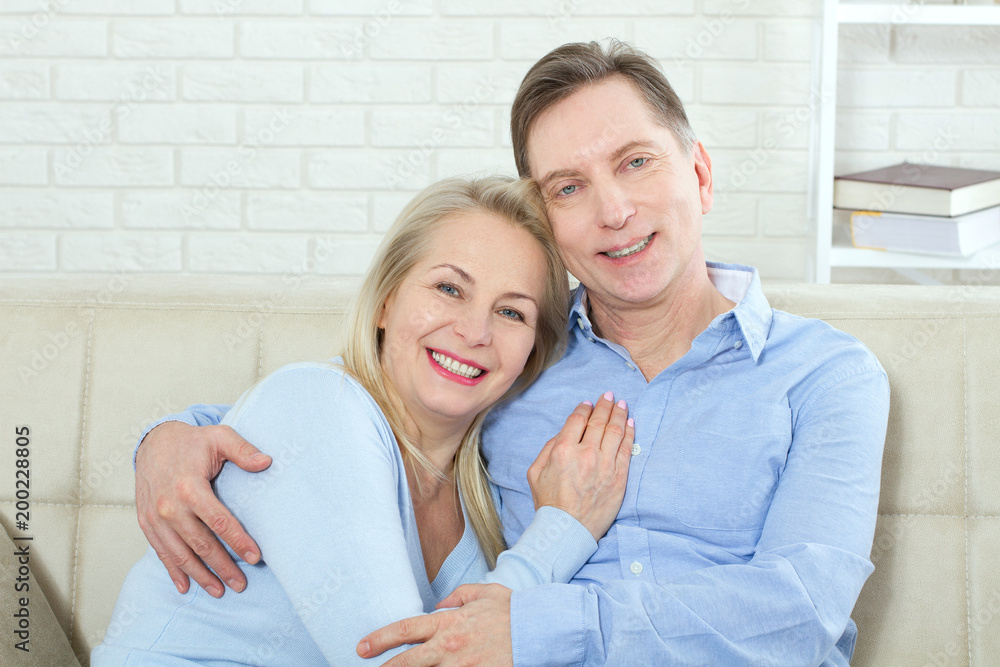 Middle aged couple relaxing on the couch smiling at camera at home in the living room Middle aged couple relaxing on the couch smiling at camera at home in the living room