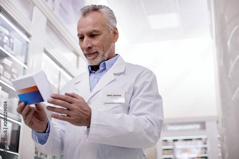 Progressive medicine. Low angle of mature pleasant male pharmacist staring down while carrying medication Progressive medicine. Low angle of mature pleasant male pharmacist staring down while carrying medication