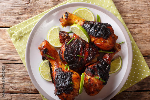 Obraz na plátně Grilled jerk chicken drumstick with lime and onions closeup on a table