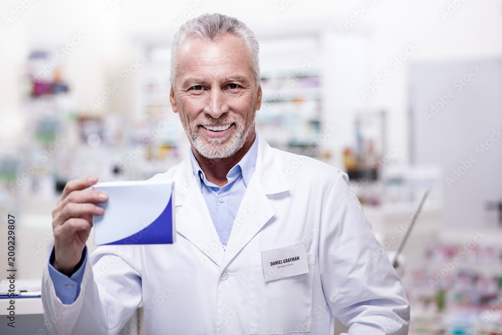 Great recommendations. Mature cheerful male pharmacist smiling while presenting medication
