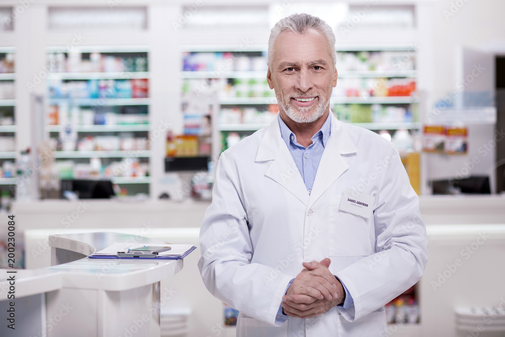 Come in. Mature joyful male pharmacist looking at camera while grinning