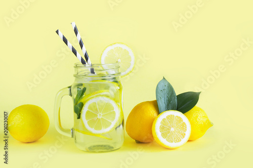 Summer lemonade with lemon, mint and ice in mason jar on yellow. Tropical concept.