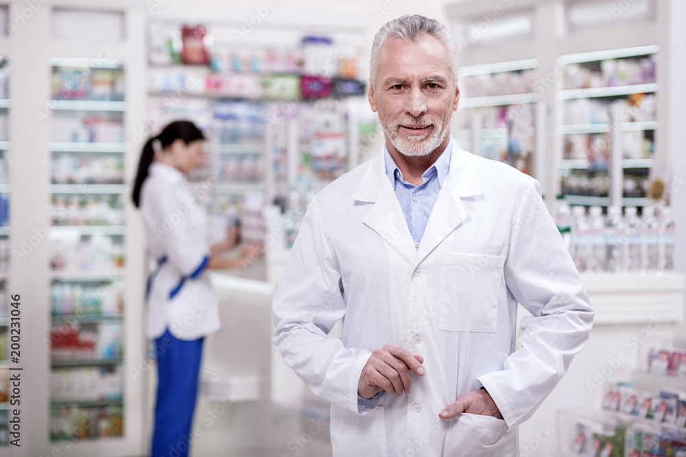 Perfect drugstore. Senior ambitious male pharmacist putting hand in pocket while looking at camera