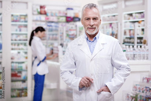 Perfect drugstore. Senior ambitious male pharmacist putting hand in pocket while looking at camera