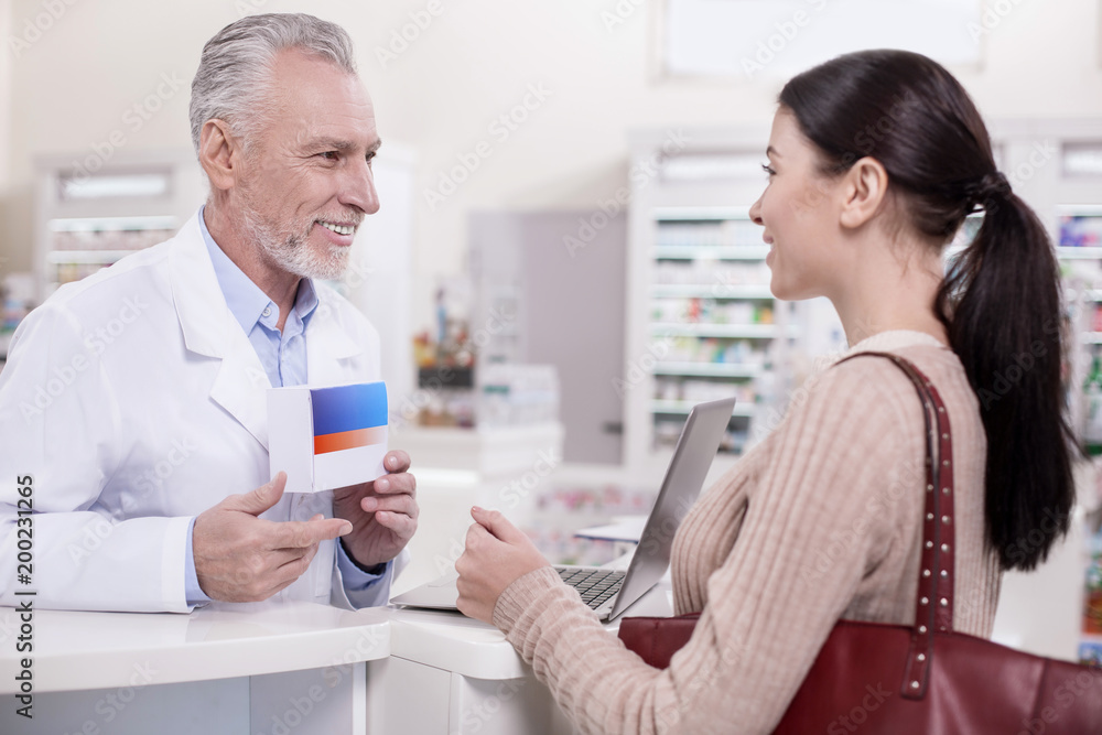 What you need. Senior joyful male pharmacist carrying drug while talking to client What you need. Senior joyful male pharmacist carrying drug while talking to client