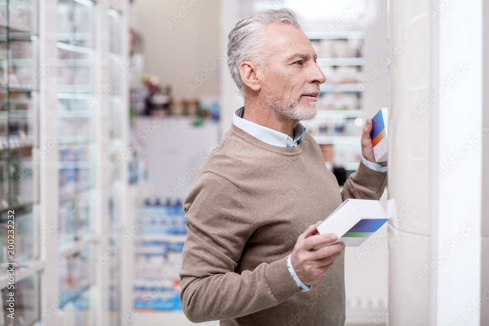 Huge difference. Focused senior man posing in profile while holding medication