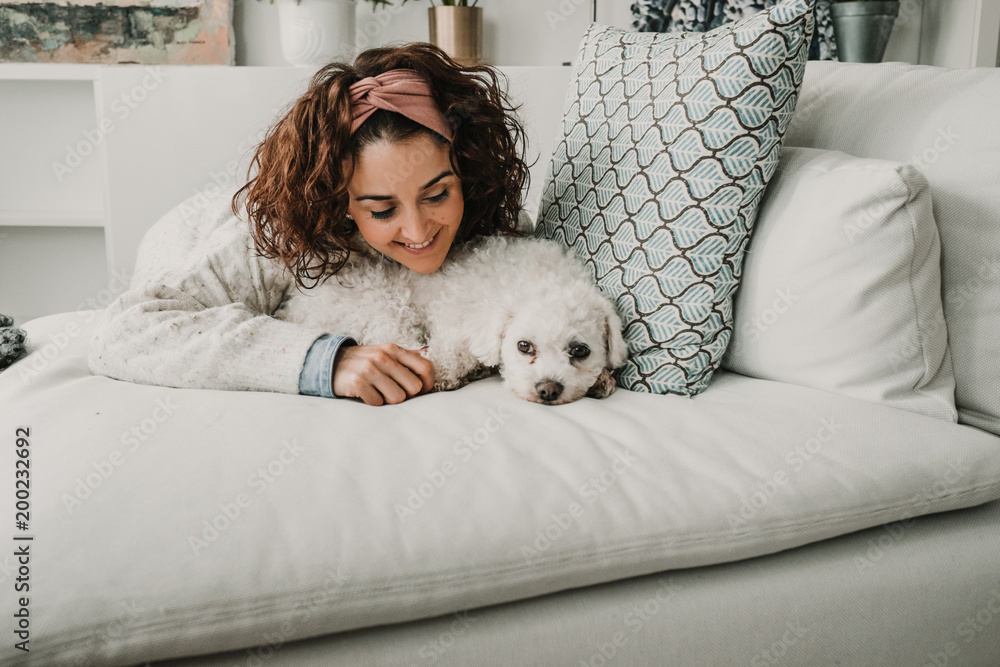 Cute little withe dog playing with her owner on the sofa of a nordic house, all in withe colors. Lifestyle indoor. Affective photography. Cute little withe dog playing with her owner on the sofa of a nordic house, all in withe colors. Lifestyle indoor. Affective photography.