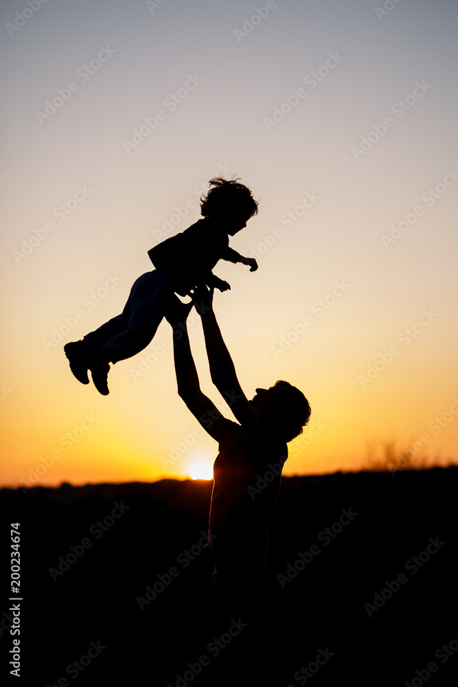 Silhouette of a man and his son playing together outdoor at sunset. Vertical photo. Family concept