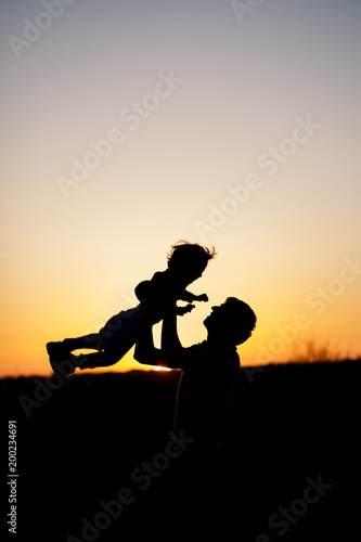 Silhouette of a man and his son playing together outdoor at sunset. Vertical photo. Family concept