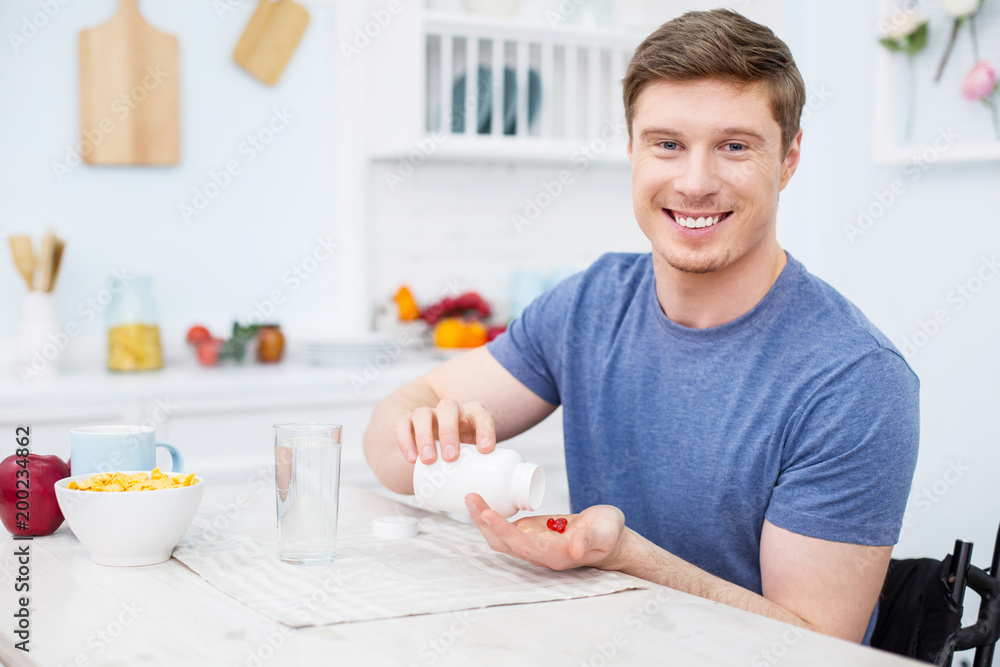 Taking vitamins. Handsome brunette keeping smile on face while looking at camera Taking vitamins. Handsome brunette keeping smile on face while looking at camera