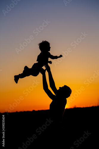 Loving father and his little son having fan together outdoors. Happy family. Fatherhood. Toddler boy and his dad playing. Family as silhouette on sunset. Vertical photo