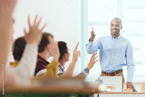 Fotografia Smiling african american teacher and schoolchildren with arms up in classroom