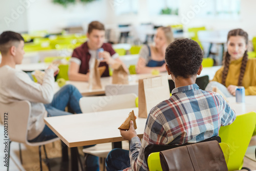 group of teen students chatting while taking lunch at school cafeteria