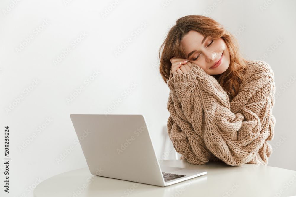 Naklejka premium Image of relaxed woman 20s with closed eyes sitting at table in cafe, and using laptop