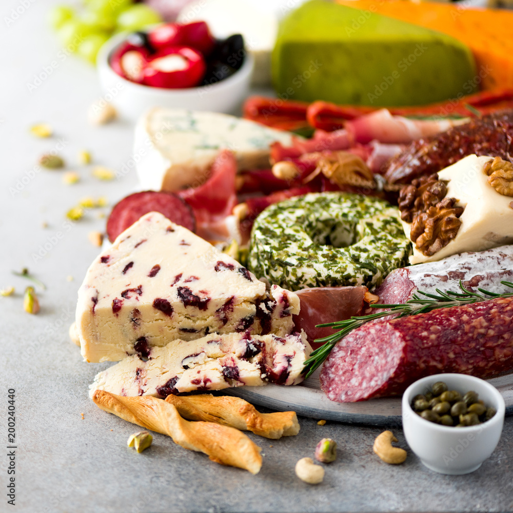 Traditional italian antipasto, cutting board with salami, cold smoked meat, prosciutto, ham, cheeses, olives, capers on grey background. Cheese and meat appetizer. Square crop