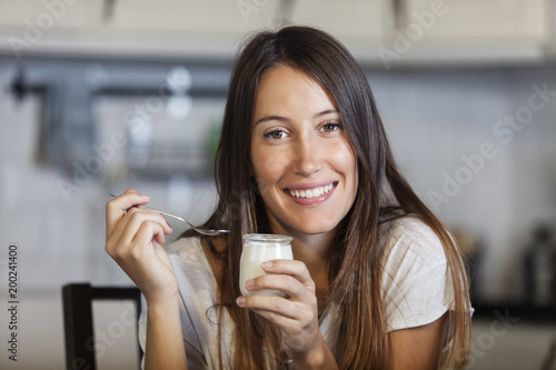 Portrait of beautiful young woman eating yogurt at home. Healthy food concept