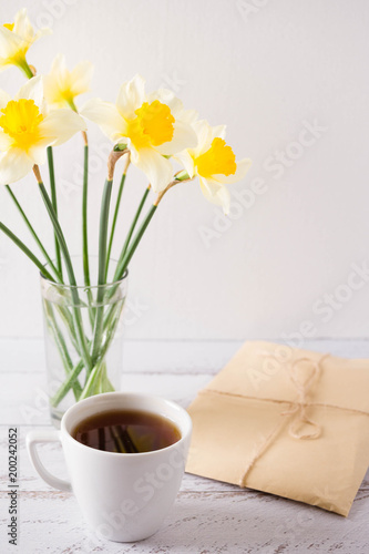 Letters in craft paper on wooden table next to tea cups and a vase with the daffodilsю Place for text