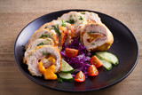 Chicken wrapped with ham and cheddar cheese; vegetables in black plate on wooden table. horizontal