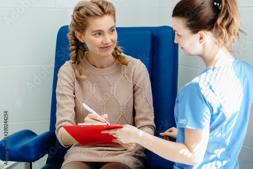 Beautyful blonde woman with two braids sitting in cabinet and to doctor consulting patient about signing paper. Insurance concept.